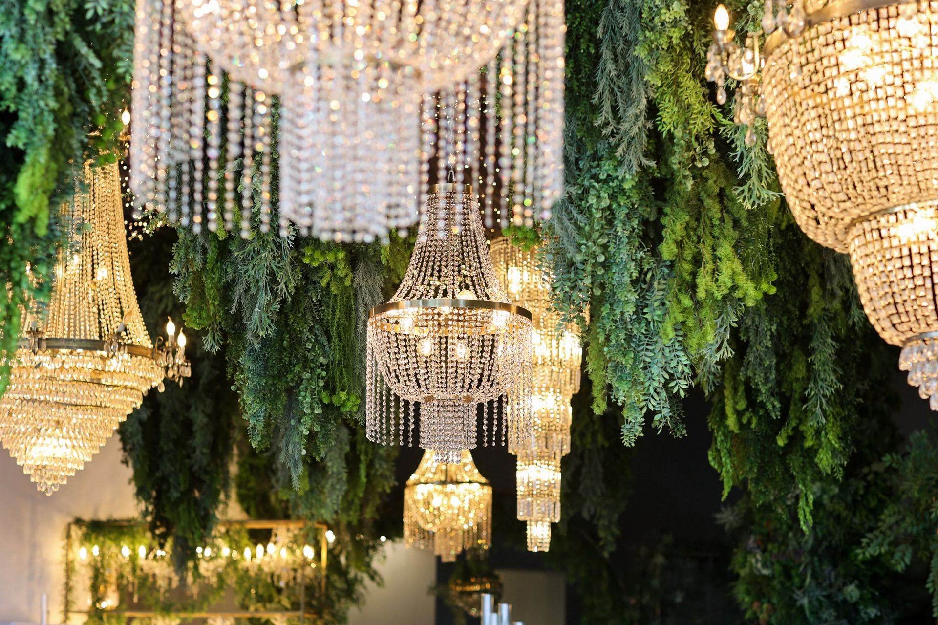 Crystal chandeliers hanging among greenery at a reception venue